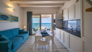 A modern kitchen with white cabinets, a dining area with a table and chairs, and a view of the sea through a sliding door. - Apartment Lights (Avola)