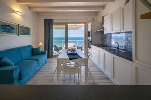 A modern kitchen with white cabinets, a dining area with a table and chairs, and a view of the sea through a sliding door. - Apartment Lights (Avola)