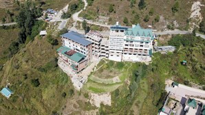 A large building with multiple floors, surrounded by greenery and a winding road. - Hardys Retreat (Shimla)