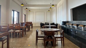 A spacious dining area with multiple wooden tables and chairs, pendant lighting, and a large kitchen counter. - Hardys Retreat (Shimla)
