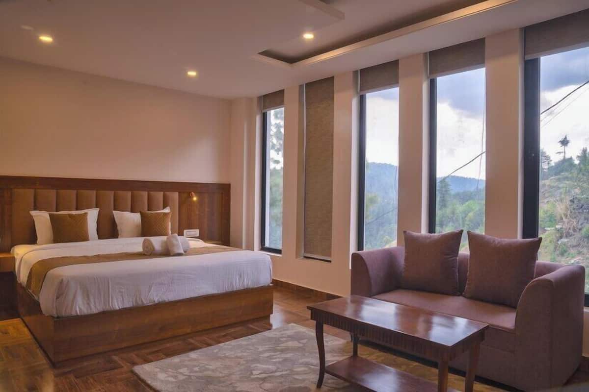A bedroom with a large bed, a sofa, a coffee table, and a view of the outdoors through large windows.
