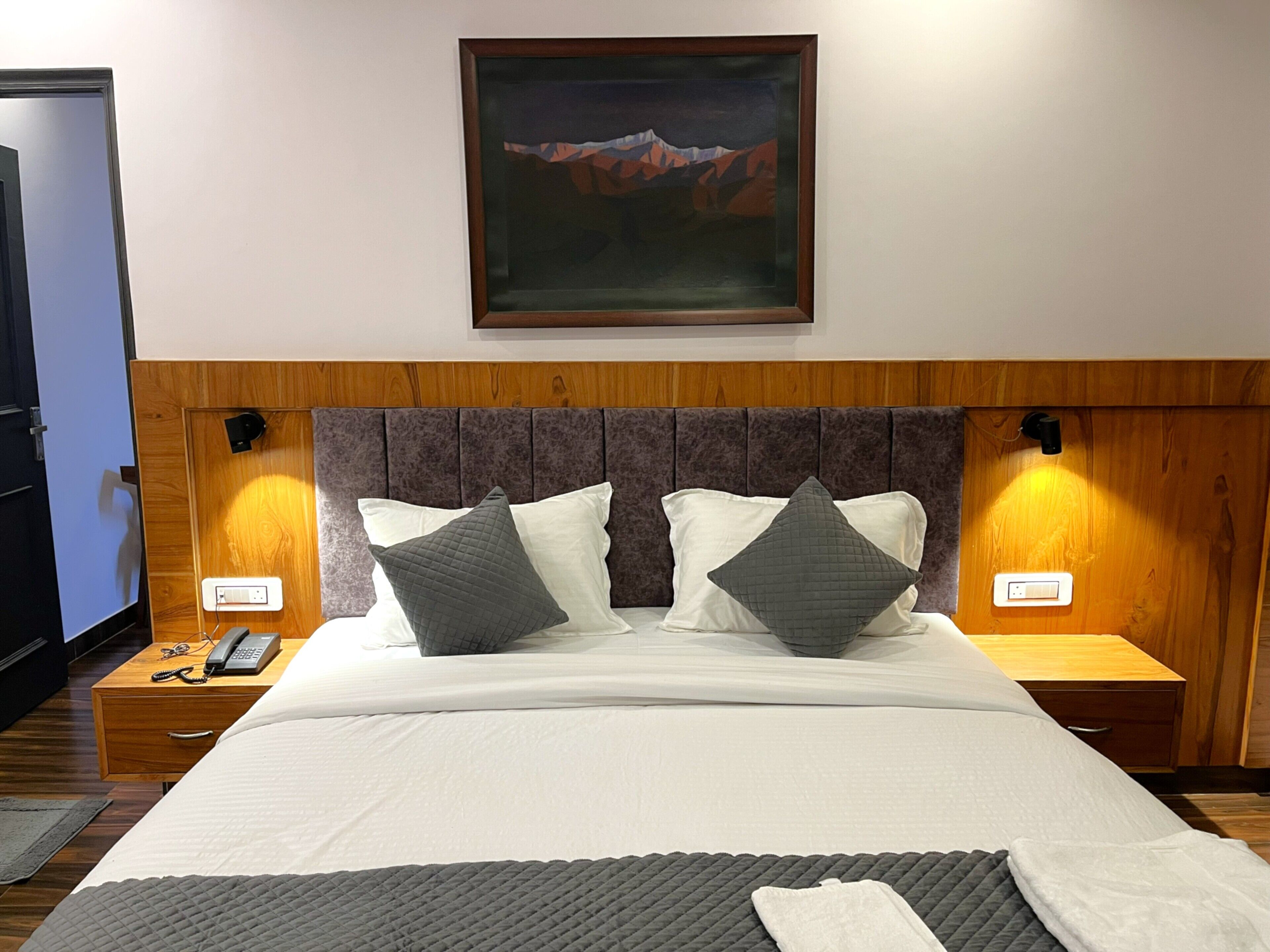 A neatly made bed with white and gray bedding, a wooden headboard, and a painting above.