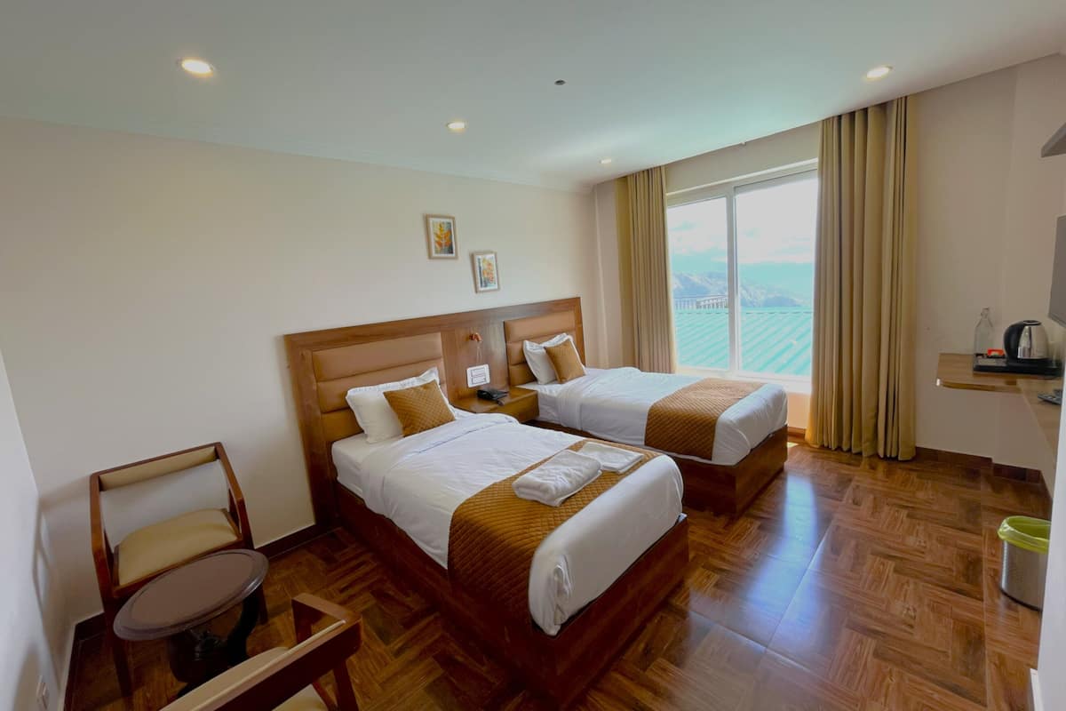 A hotel room with two beds, a chair, a small table, a TV, and a view of the mountains.