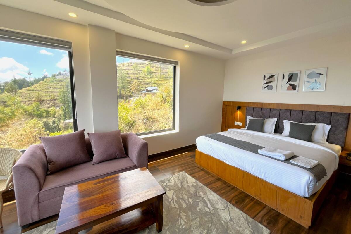 A bedroom with a large bed, a sofa, and a view of a hilly landscape.