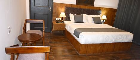 A hotel room with a wooden bed, two bedside tables with lamps, a chair, and a wooden floor.
