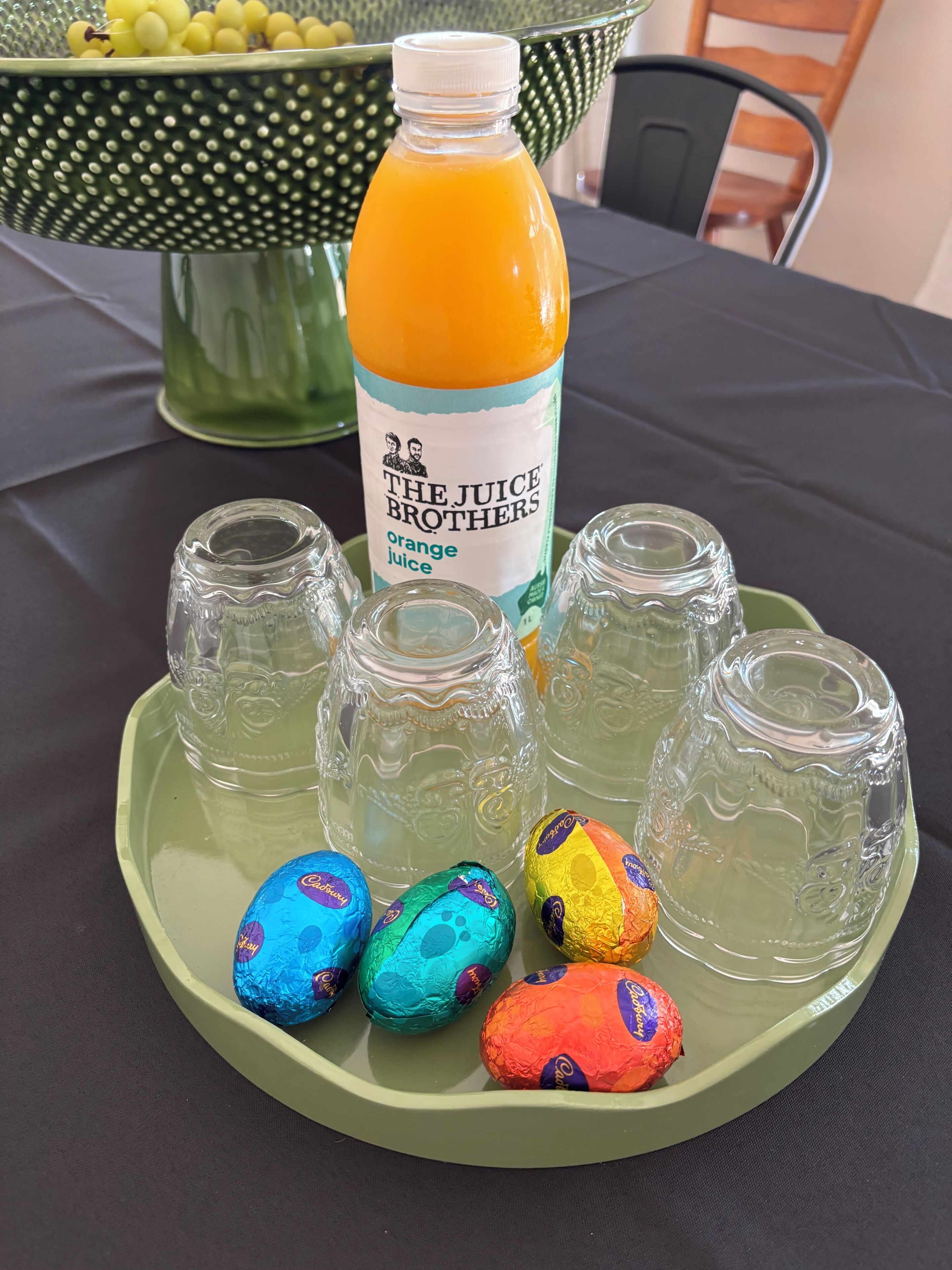 Une table avec une bouteille de jus d’orange, des verres vides et des chocolats emballés.