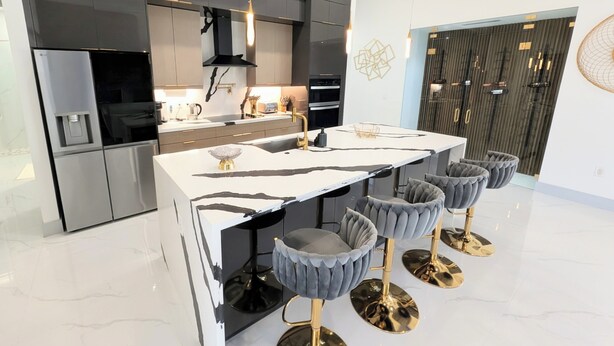 Een moderne keuken met een centraal eiland, barkrukken en een eethoek.