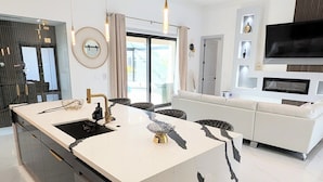 Een moderne keuken met een centraal kookeiland, een zithoek met een bank en een woonkamer met een televisie.