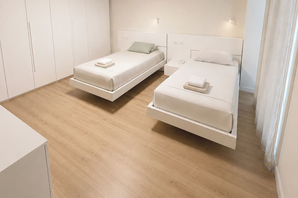 A modern bedroom with two beds, a wardrobe, and a ceiling light.