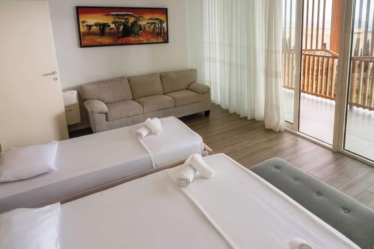 A hotel room with a bed, a sofa, a painting, and a balcony with a view.