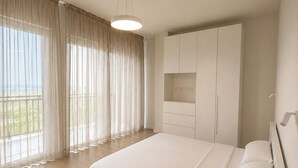 A bedroom with a large bed, a wardrobe, a built-in TV shelf, and a view of the outdoors.