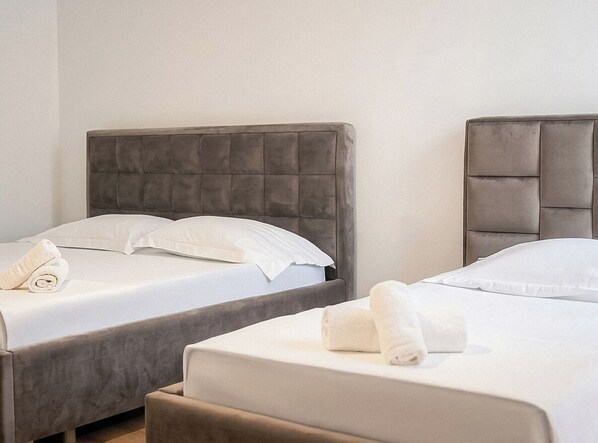 Two twin beds with grey upholstered headboards, white linens, and rolled towels. - Stay By Ilvesta Green Coast 49B (Himare)