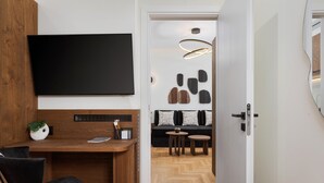 A modern living room with a flat-screen TV, wooden furniture, a sofa with patterned cushions, and a unique wall art installation. - Voukourestiou Signature Suite (Athens)
