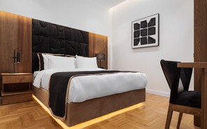 Une chambre moderne avec une tête de lit en bois, un grand lit avec une literie blanche, une table de chevet, une chaise et une œuvre d’art abstraite encadrée accrochée au mur.