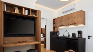 A modern kitchen with wooden cabinetry, a built-in TV, and a small dining area with stools. - Voukourestiou Signature Suite (Athens)