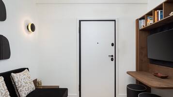 Una habitación moderna con un sofá negro, una puerta blanca, un televisor montado en la pared y una estantería con libros.