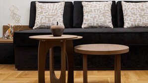 A modern living room with a black sofa, patterned cushions, a round wooden table with a bowl, and abstract wall art. - Voukourestiou Signature Suite (Athens)