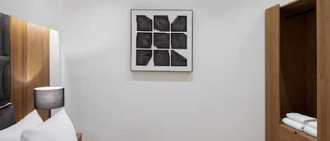 Un dormitorio moderno con una cama, una mesita de noche, una lámpara, un armario de madera y una obra de arte abstracta enmarcada en la pared.