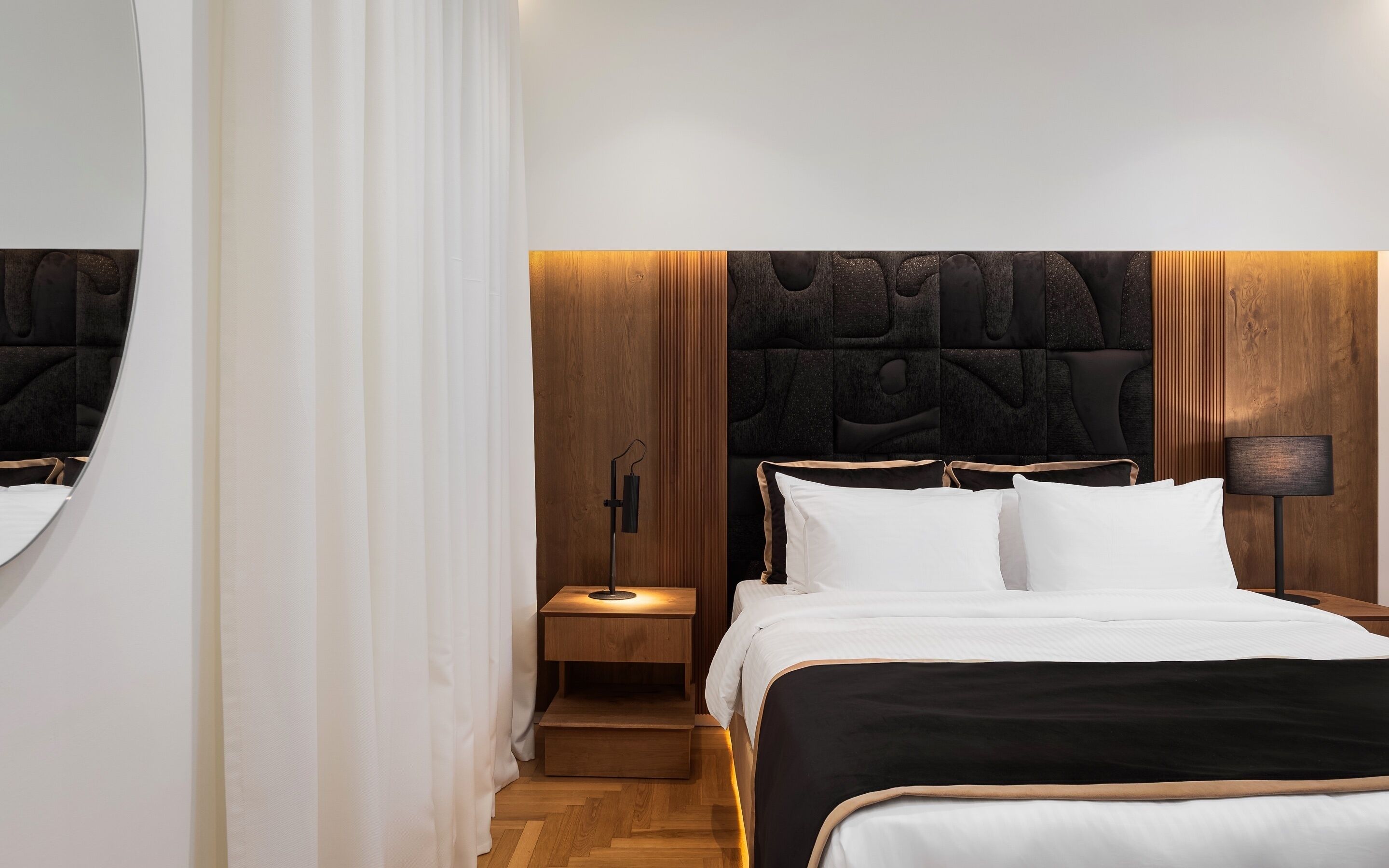 Habitación de hotel moderna con una cama grande, cabecera de madera y una mesita de noche con lámpara.