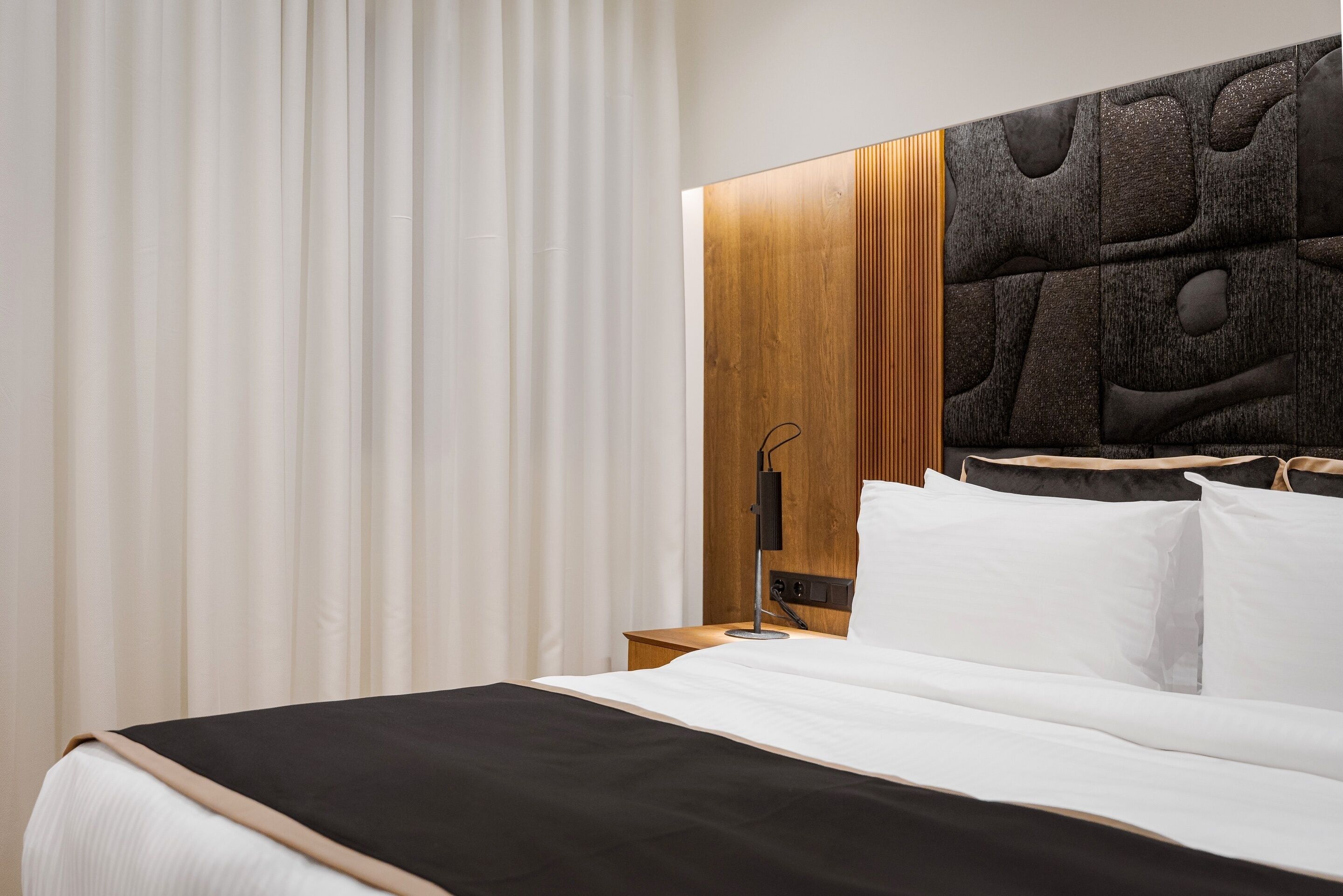 Une chambre d’hôtel moderne avec un grand lit, une tête de lit en bois et une table de chevet avec une lampe.