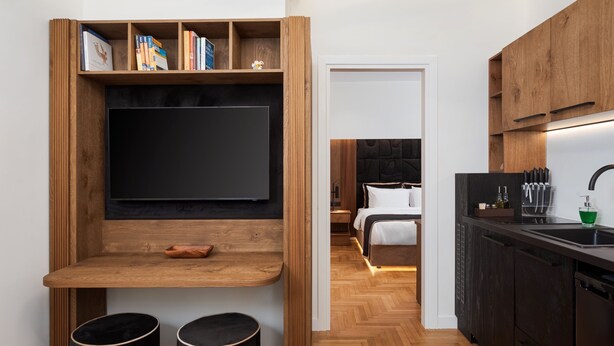 A modern kitchen with wooden cabinetry, a black countertop, and a built-in TV. - Voukourestiou Signature Suite (Athens)