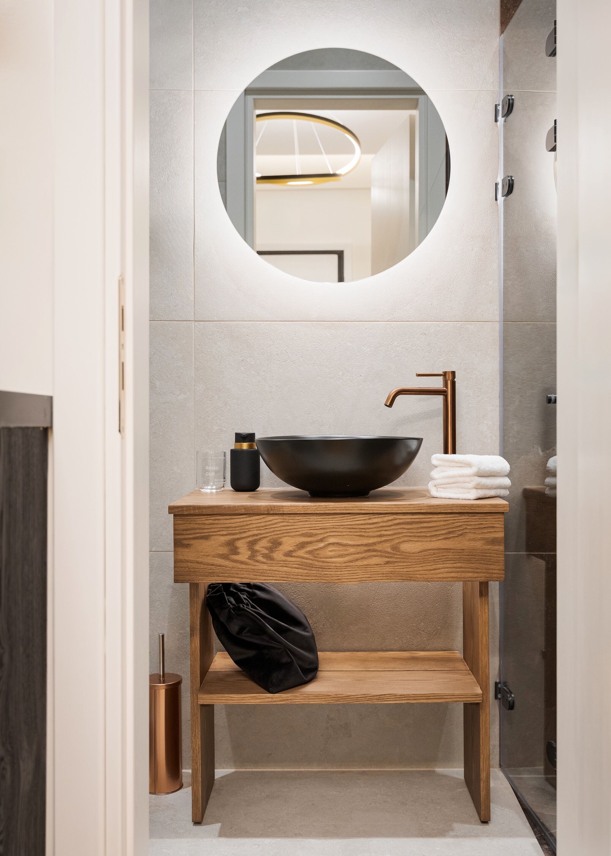 A modern bathroom with a wooden vanity, a black bowl sink, and a round mirror.