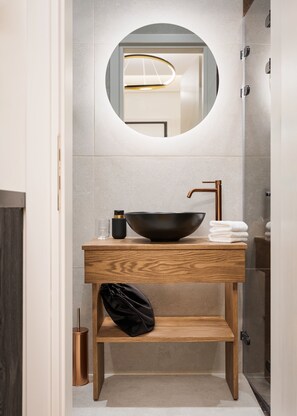 Une salle de bain moderne avec un meuble-lavabo en bois, un lavabo noir en forme de bol et un miroir rond.