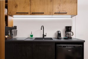 Une cuisine moderne avec des meubles en bois, un plan de travail noir, un évier, une machine à café et un lave-vaisselle.
