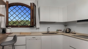 A modern kitchen with white cabinets, a dishwasher, a sink, a window with a view of greenery, and a bar stool. - Classic villa, Cala di Volpe, minutes away from Sardinia's most iconic beaches (Sardegna)
