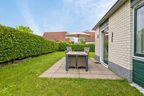 A patio with a table and chairs, a hedge, and a building with a brick facade. - Stay at Holiday Home Schoneveld 249 at Holiday Park Schoneveld. This dog-friendly property has an enclosed garden and a bedroom downstairs. (Breskens)