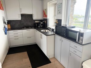 A compact kitchen with white cabinets, a black countertop, a stove, a sink, a coffee maker, and a microwave. - This charming two-room apartment in Port Scaldis (no. 19-42) offers a unique combination of sea and countryside views, making it perfect for a relaxing holiday on the Zeeland coast. (Breskens)