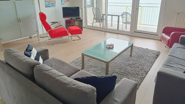 Ett modernt vardagsrum med en soffa, röda fåtöljer, ett soffbord i glas och en tv.