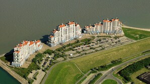 Ett högt hotell med flera balkonger, en parkeringsplats och utsikt över stranden.