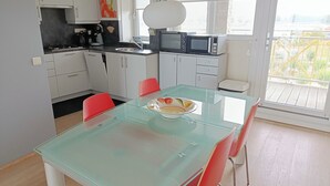 Ett modernt kök med vita skåp, ett glasbord och röda stolar.