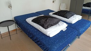 En dubbelsäng med blått sänglinne och två svarta kuddar, ett litet runt bord och en väggmonterad lampa.