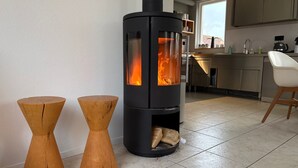 Eine moderne Küche mit Holzofen, zwei hölzernen Barhocker und einem weißen Stuhl.