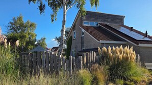 Ein zweistöckiges Haus mit geneigtem Dach, einem Holzzaun und hohem Gras im Vordergrund.