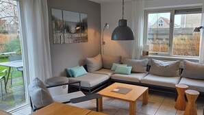 Ein gemütliches Wohnzimmer mit einem Ecksofa, einem Holztisch und einer schwarzen Pendelleuchte.
