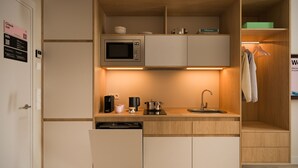 Una kitchenette compacta con microondas, cafetera y lavamanos, además de un mueble de madera en la parte superior.