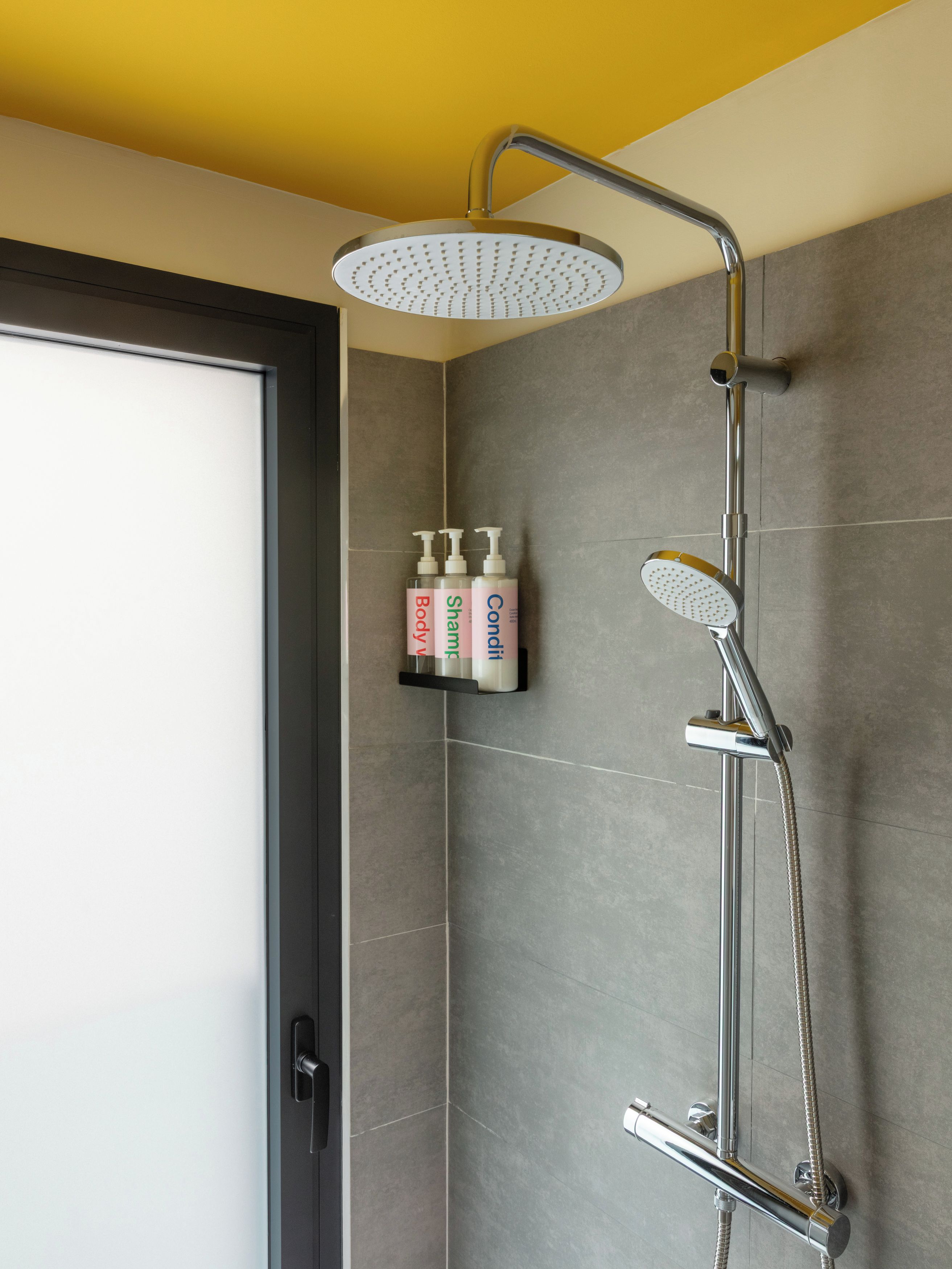 A shower with a handheld showerhead and a wall-mounted rain showerhead, a towel rack, and a shelf with toiletries.