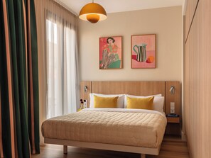 Une chambre d’hôtel comprenant un lit, une table de chevet, une lampe fixée au mur et deux œuvres d’art encadrées.