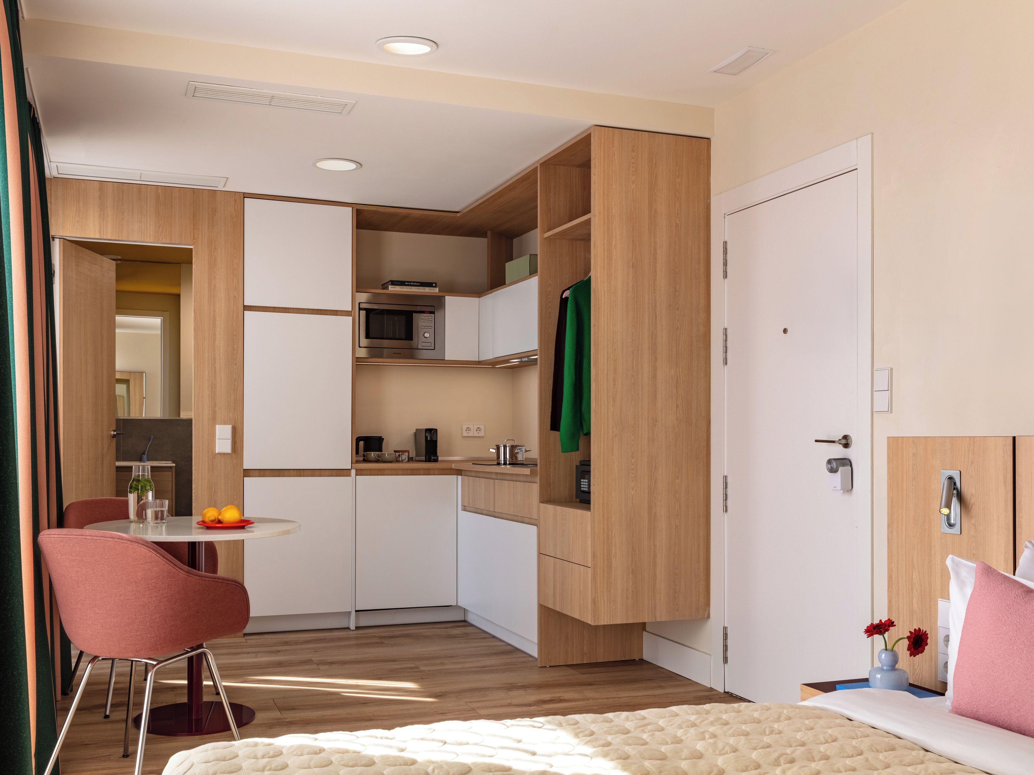 A compact hotel room with a kitchenette, a dining area, and a bed.