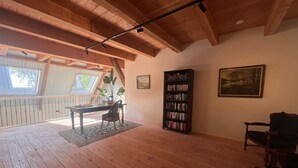 Ein Zimmer mit Holzböden, einem Bücherregal, einem Tisch mit Stühlen, einem Bild an der Wand und einem Fenster.