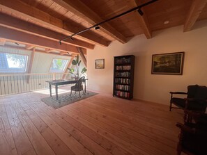 Ein Zimmer mit Holzböden, einem Bücherregal, einem Tisch mit Stühlen, einem Bild an der Wand und einem Fenster.