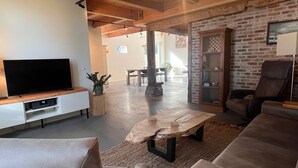 Ein modernes Wohnzimmer mit Flachbildfernseher, bequemen Sitzmöglichkeiten, einem Holztisch und einer Ziegelwand.