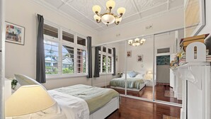 Un dormitorio con cama, mesita de noche, lámpara, espejo y ventana con cortinas.