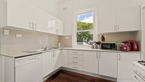 Una cocina moderna con armarios blancos, lavavajillas, microondas y un hervidor rojo.