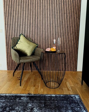 Ein Zimmer mit einer Wand aus Holzlatten, einem gepolsterten Sessel, einem kleinen runden Tisch mit Drahtgestell und einem schwarzen Teppich auf dem Boden.