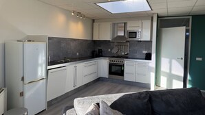 Een kleine keuken met een magnetron, fornuis en spoelbak. Er is een plafondlamp en een dakraam.