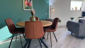 Een moderne vergaderruimte met een ronde houten tafel, bruine leren stoelen, een kleurrijk abstract schilderij en een potplant op de vensterbank.